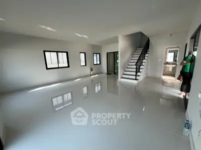 Spacious modern living room with sleek staircase and glossy tiled floors.