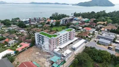 Aerial view of modern apartment building near scenic coastline with lush greenery and ocean backdrop.