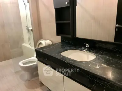 Modern bathroom with sleek black marble countertop and glass shower enclosure.