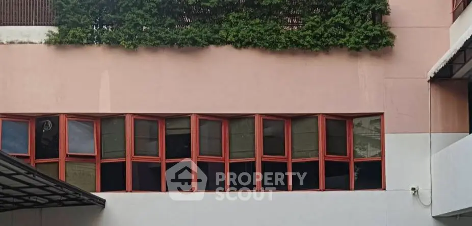 Modern building exterior with unique red-framed windows and lush greenery
