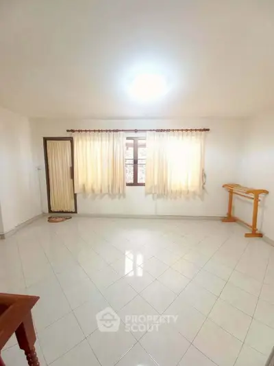 Spacious empty room with tiled floor and large window, perfect for customization.