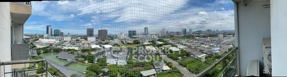 Panoramic city view from high-rise balcony with expansive skyline and lush greenery.