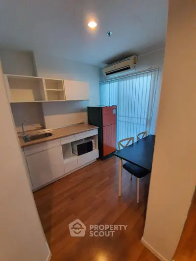 Modern kitchen with sleek cabinetry, dining table, and air conditioning in a cozy apartment setting.