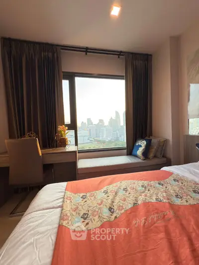 Cozy bedroom with city view, featuring a stylish desk and comfortable seating by the window.