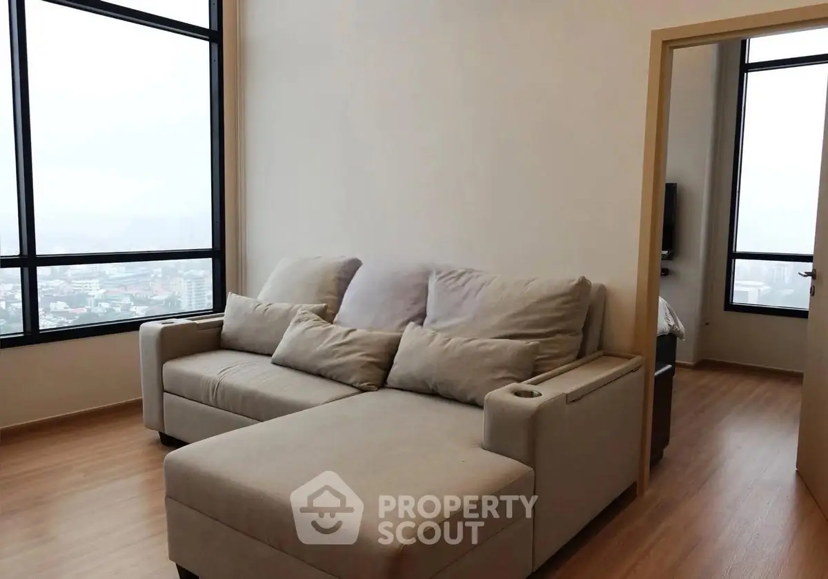 Modern living room with large windows and cozy sofa in high-rise apartment.