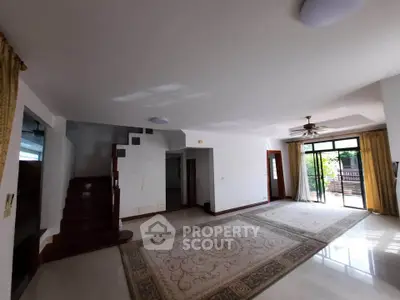 Spacious living room with elegant staircase and large windows opening to a garden view.