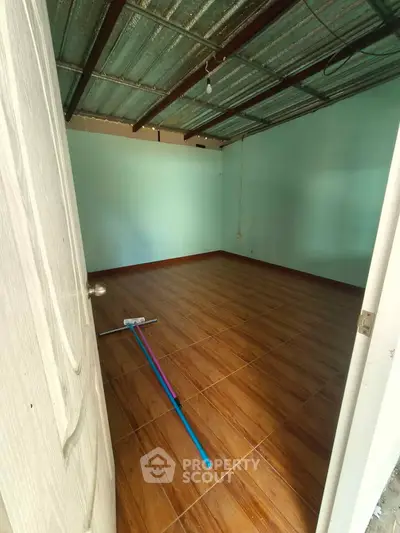 Spacious empty room with wooden flooring and metal ceiling, ready for customization.