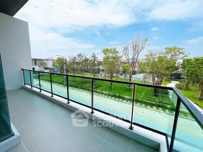 Spacious balcony with glass railing offering serene garden views in modern residential complex.
