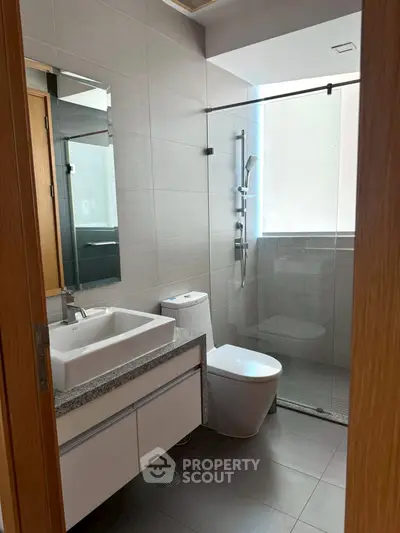 Modern bathroom with sleek fixtures and glass shower enclosure in contemporary apartment.