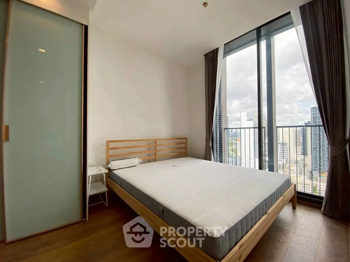Modern bedroom with large windows and city view, featuring a minimalist design and wooden flooring.