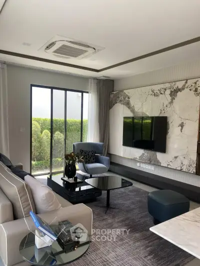 Luxurious living room with modern decor, marble accent wall, and large windows overlooking greenery.