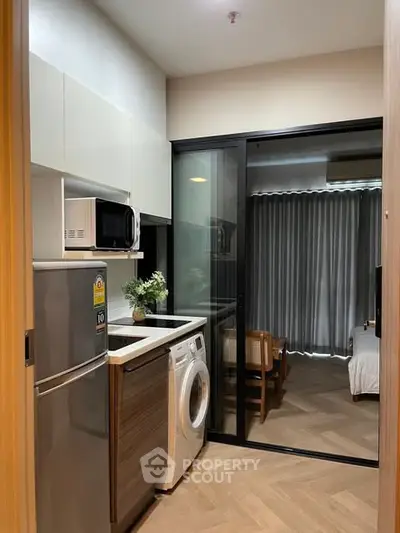 Modern compact kitchen with washing machine and microwave, adjacent to cozy living area with wooden flooring.