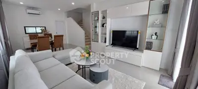 Modern living room with sleek furniture and open dining area, featuring a stylish staircase.