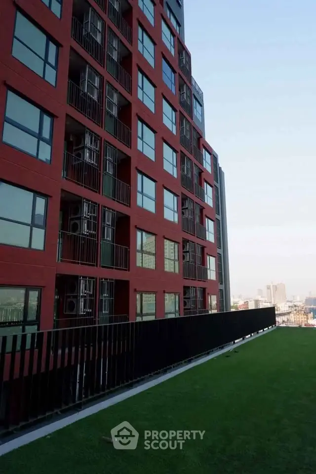 Modern red brick apartment building with city view and green rooftop terrace.