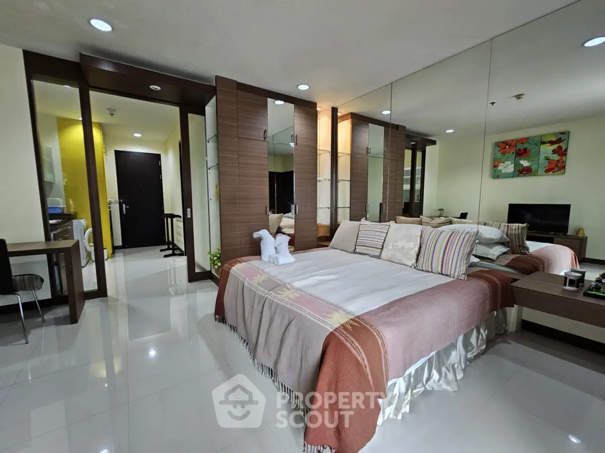 Spacious bedroom with modern decor and mirrored wall, featuring cozy bedding and stylish furnishings.