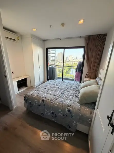 Cozy bedroom with balcony offering stunning city view, featuring modern decor and ample natural light.