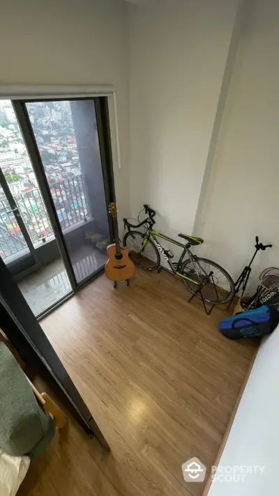 Cozy room with wooden flooring, balcony access, guitar, and bicycle storage.