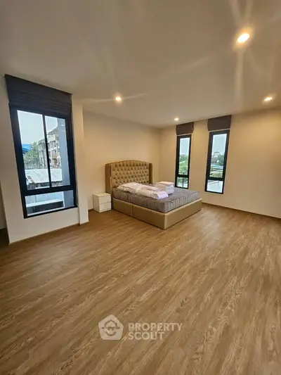 Spacious bedroom with large windows and wooden flooring in modern apartment