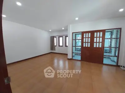 Spacious empty room with wooden flooring and glass doors, perfect for customization.