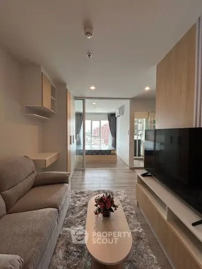 Modern living room with cozy sofa, TV, and view into stylish bedroom