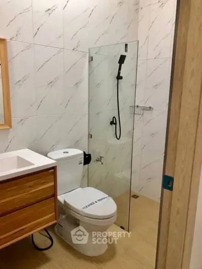 Modern bathroom with glass shower and wooden vanity in stylish apartment.