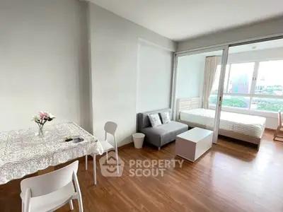 Modern studio apartment with open layout and wooden flooring, featuring a cozy living area and bright bedroom.