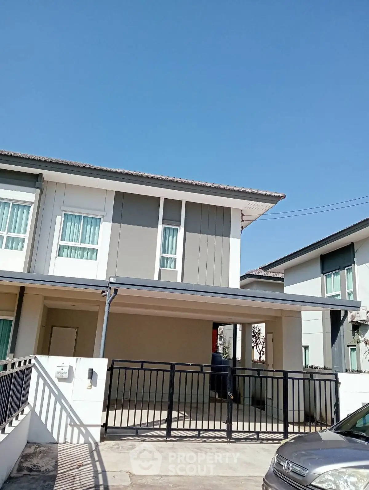 Modern two-story house with gated driveway and clear blue sky backdrop.