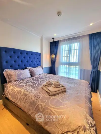 Elegant bedroom with plush blue headboard and natural light through large window.