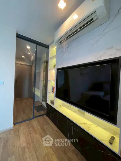 Modern living room with sleek TV unit and glass partition, featuring elegant wood flooring and ambient lighting.