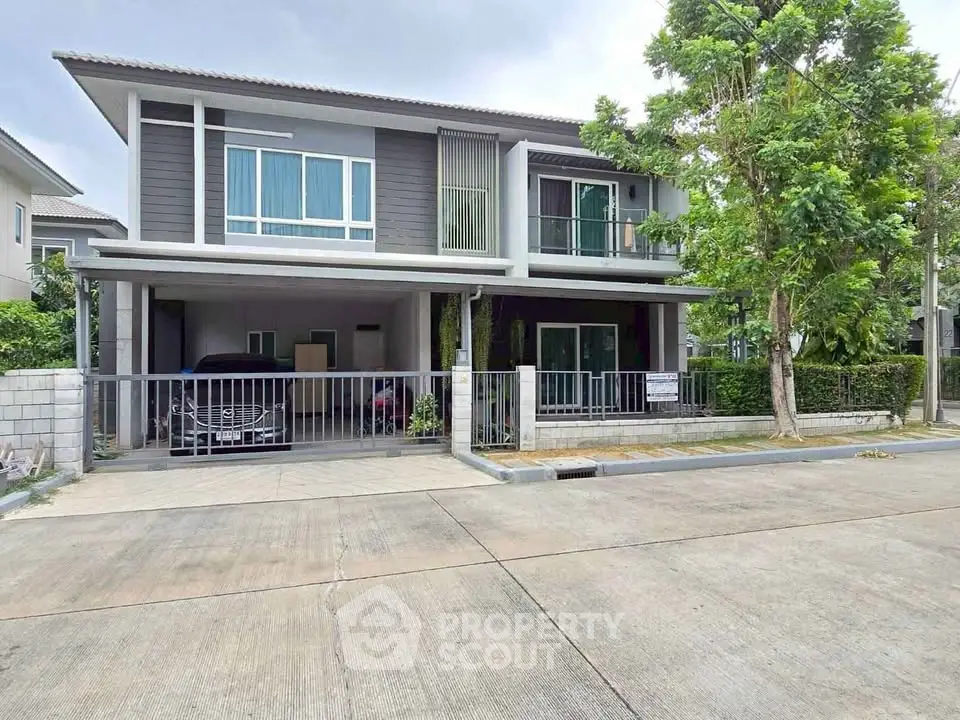Modern two-story house with carport and lush greenery in a serene neighborhood.
