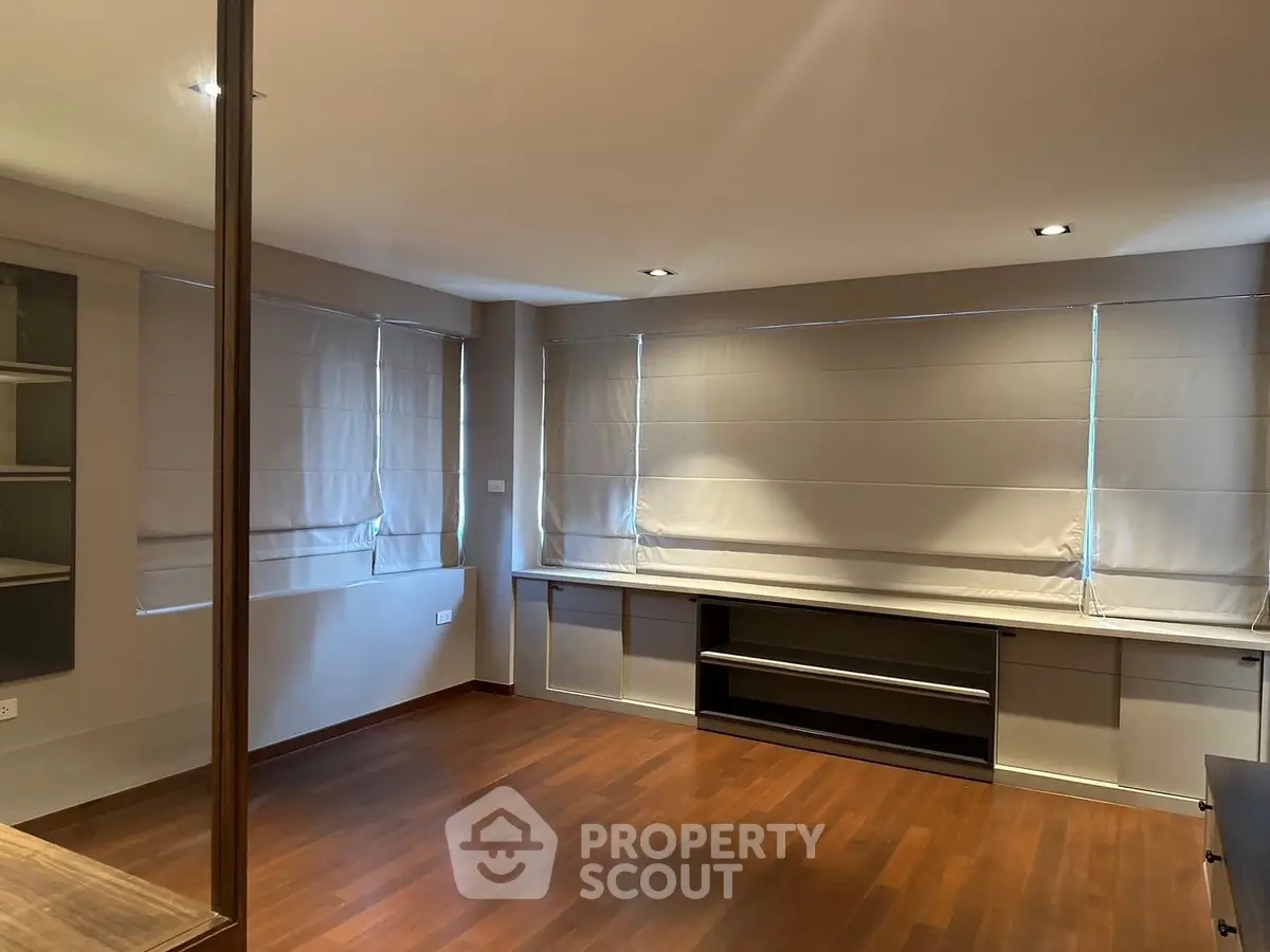 Spacious empty room with wooden floors and large windows, ideal for customization.