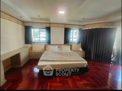 Spacious bedroom with elegant wooden flooring and large windows for natural light.