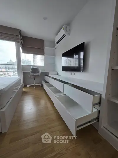 Modern bedroom with sleek white furniture, wall-mounted TV, and city view from large windows.