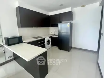 Modern kitchen with sleek black cabinets, fridge, and washing machine in open layout.