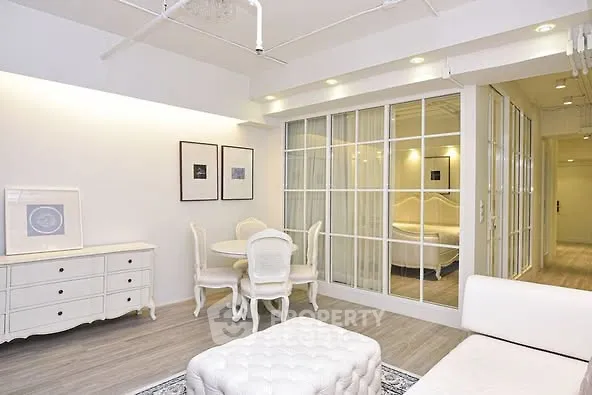 Elegant living room with white furniture and glass partition showcasing a cozy bedroom.