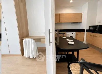 Modern kitchen with wooden cabinets and black countertops, featuring a washing machine and dining area.