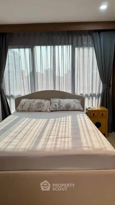 Cozy bedroom with large windows and elegant curtains, featuring a comfortable bed and stylish decor.