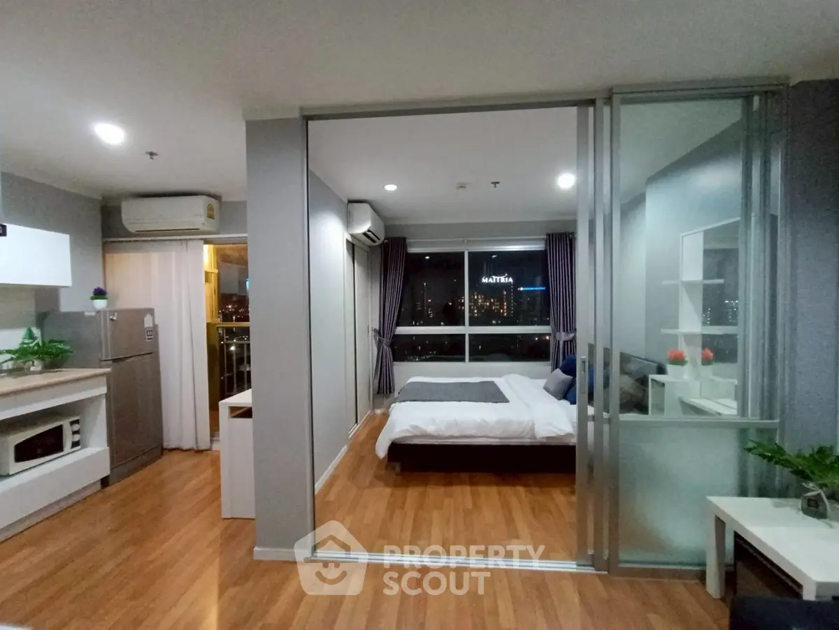 Modern studio apartment with open layout and city view, featuring sleek kitchen and cozy bedroom.