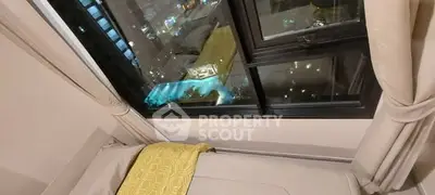 Cozy bedroom with city view and pool from window, featuring elegant curtains and bedding.