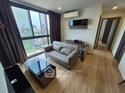 Modern living room with large window and city view, featuring sleek furniture and wooden flooring.