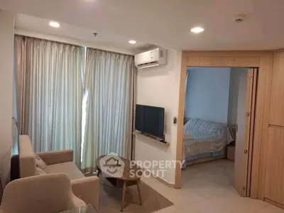 Modern living room with cozy sofa, wall-mounted TV, and adjacent bedroom in open layout apartment.