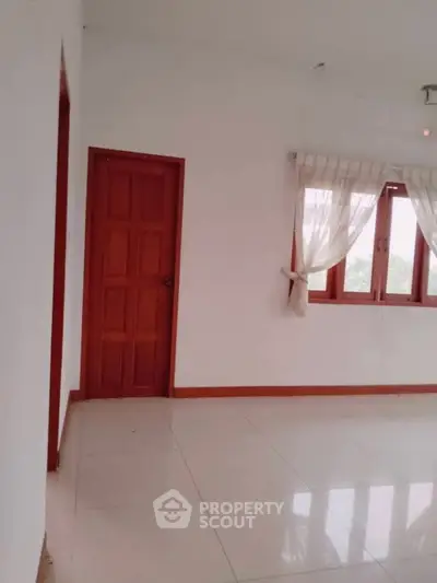 Spacious room with white walls, tiled floor, and wooden door and window frames.