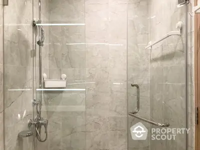 Elegant marble-tiled bathroom with glass shower enclosure and modern fixtures, showcasing a luxurious and serene bathing space.