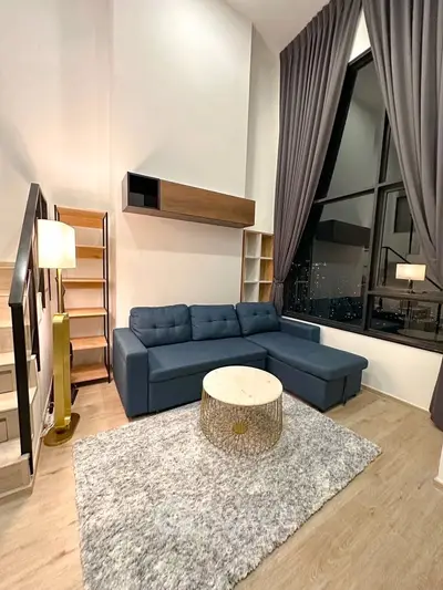 Modern living room with high ceilings, stylish furniture, and large windows offering city views.