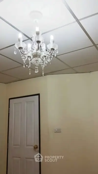 Elegant chandelier in a minimalist room with white door and ceiling tiles.