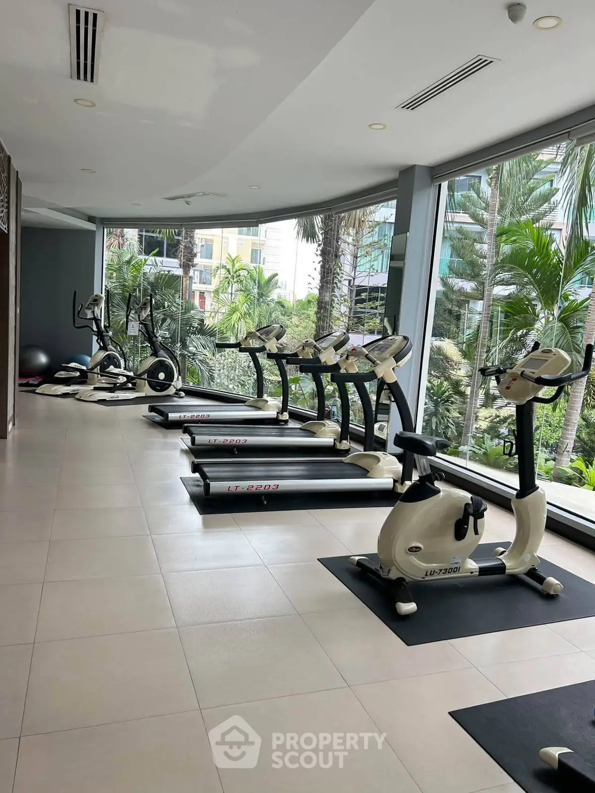 Modern gym with large windows and lush garden view, featuring treadmills and exercise bikes.
