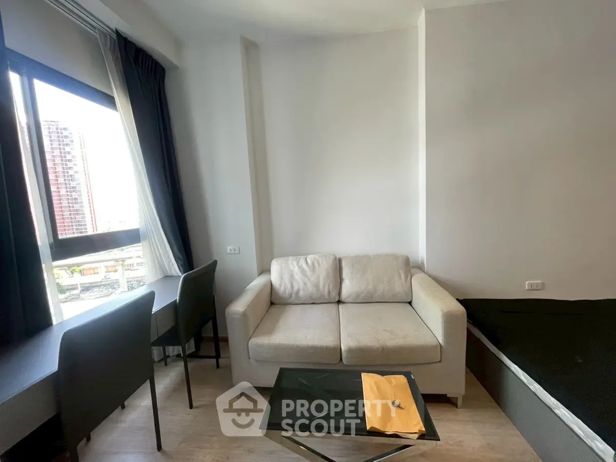 Modern studio apartment with cozy sofa, large window, and city view.