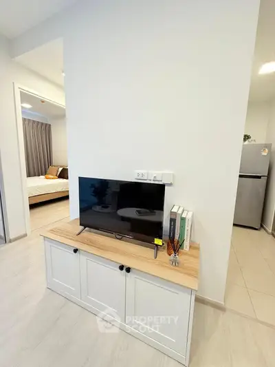 Modern living space with TV unit and glimpse of bedroom and kitchen