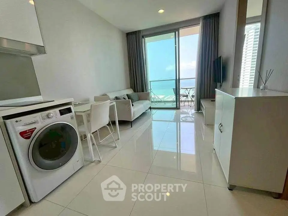 Modern living room with ocean view, sleek furniture, and washing machine in a high-rise apartment.