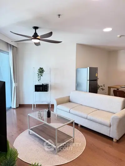 Modern living room with ceiling fan, cozy sofa, and sleek glass coffee table in a bright apartment.